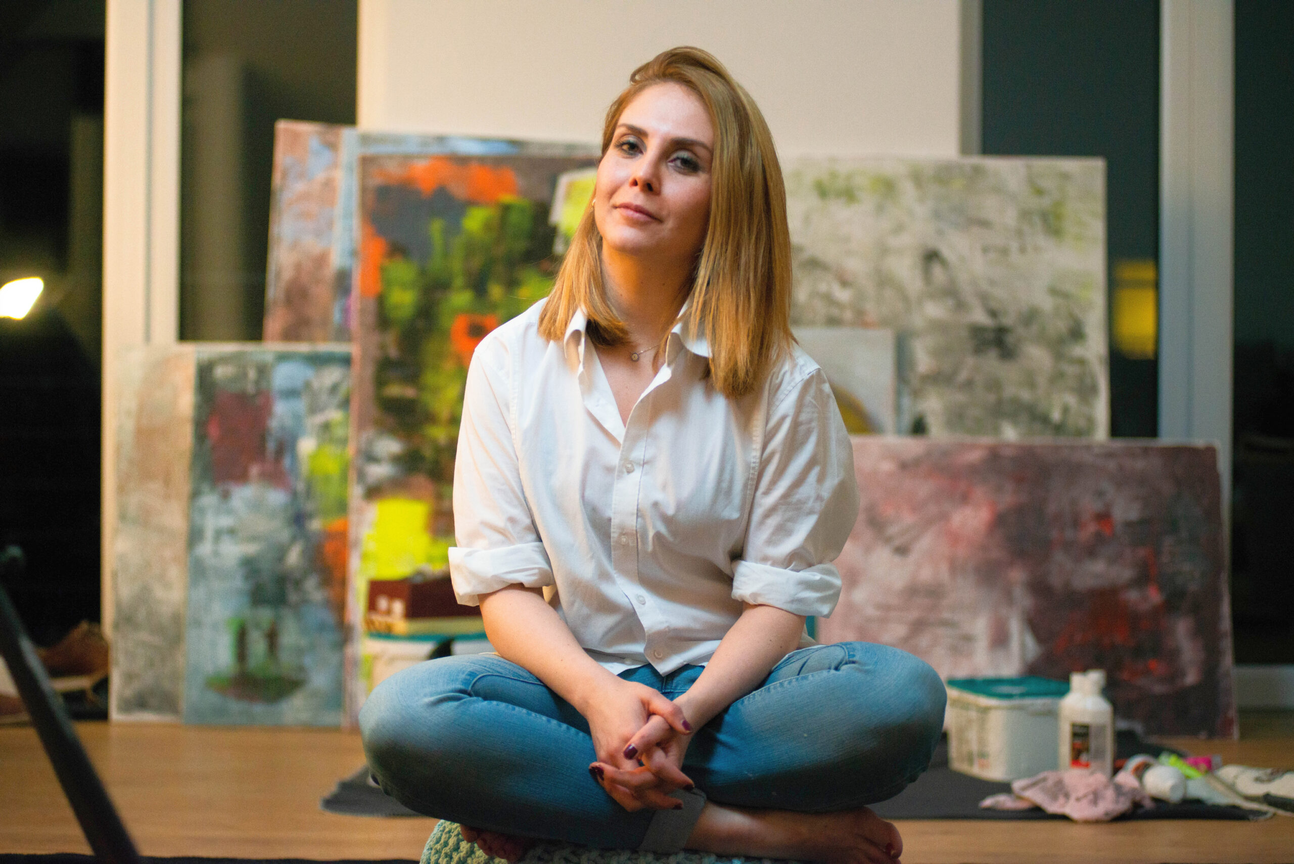 Die Künstlerin Khadija Batti im Schneidersitz vor ihren Gemälden.